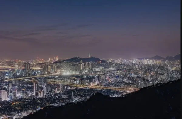 Seoul Autumn Hiking — panoramic night view of Seoul city lights seen from Achasan Mountain, including Namsan Tower and Han River bridges.